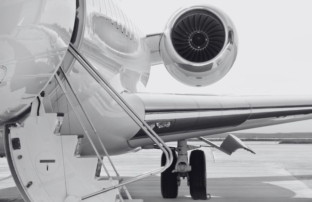 Close-up of a private jet on the ground, showing the engine, rear wing, and boarding stairs, with the landing gear visible on the tarmac.